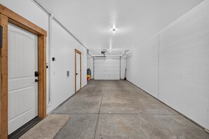 A clean, well-lit hallway with white walls and a concrete floor, leading to a garage area with a door and a hose. - Big Dipper- Downtown Greystone by the lake with air conditioning (McCall)