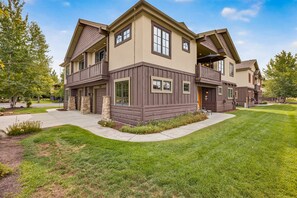 A two-story residential building with a stone foundation, a covered front porch, and a landscaped front yard. - Big Dipper- Downtown Greystone by the lake with air conditioning (McCall)