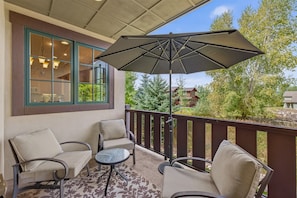 Un patio couvert avec des sièges d’extérieur, un grand parasol et une vue sur un quartier résidentiel.