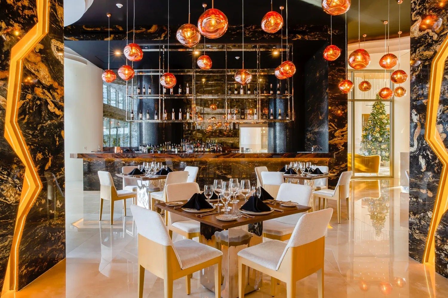 A bar area with a wine rack, seating with tables, and hanging spherical light fixtures.