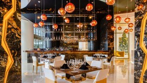 Uma área de bar com adega, assentos com mesas e luminárias esféricas penduradas.