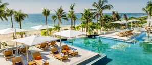 A resort pool area with lounge chairs and umbrellas, surrounded by palm trees and a view of the ocean. - Cancun All-Inclusive, Adults Only, Ocean Front Luxury Resort (Cancún)