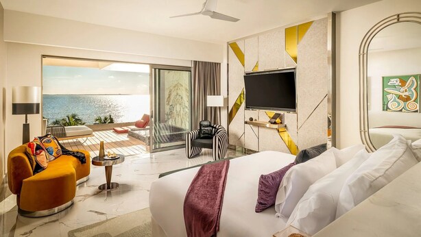 Quarto de hotel com cama, televisão, varanda vista para o mar e design de interiores moderno.
