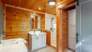 Un baño con paneles de madera, un tocador blanco, una ducha y una puerta que da a otra habitación.