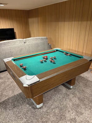 A pool table with balls and cues, a sofa, and a television in a room with wooden paneling.