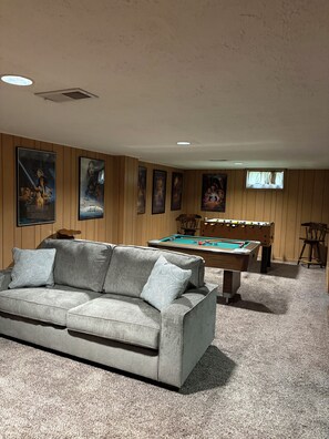 A room with a pool table, a sofa, and movie posters on the wall.