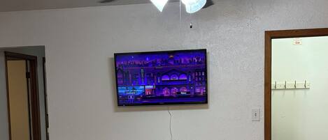 Un coin repas doté d’un ventilateur de plafond, d’un téléviseur fixé au mur et d’une table à manger en bois avec des chaises.
