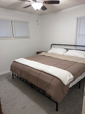 Een slaapkamer met een bed, een plafondventilator en een raam met zonwering.