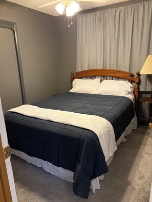 A neatly made bed with a wooden headboard, a bedside table with a lamp, and a ceiling fan.