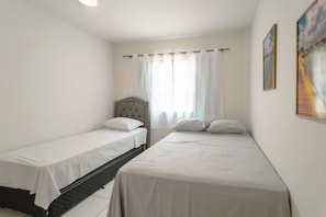 A room with two single beds, a headboard, a window with curtains, and a painting on the wall. - Budget Apartment in Zona 7 Maringa - AL09 (Maringá)
