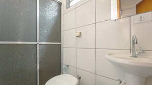 Une salle de bain avec des toilettes blanches, un lavabo et un espace douche.
