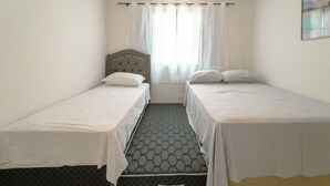 Une chambre avec deux lits simples, une fenêtre avec des rideaux et une vue sur l’extérieur.