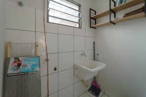 A bathroom with white tiled walls, a window, a sink, and a shelf with towels.