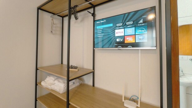 Une chambre d’hôtel équipée d’un téléviseur fixé au mur, qui permet d’accéder à différents services de diffusion en continu, d’une étagère en bois et d’une télécommande posée sur le sol.