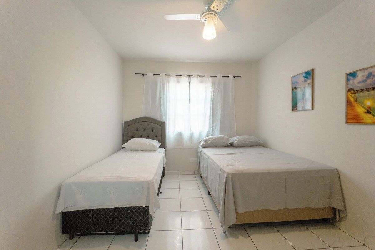 Un dormitorio con dos camas individuales, ventilador de techo y ventana con cortinas.
