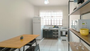 Une cuisine compacte comprenant une table à manger, des chaises, un réfrigérateur, un four à micro-ondes et une fenêtre avec des rideaux.