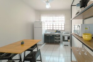 A compact kitchen with a dining table, chairs, a refrigerator, a microwave, and a window with curtains. - Budget Apartment in Zona 7 Maringa - AL09 (Maringá)