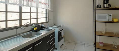 Una cocina con ventana, pileta, estufa, microondas y cafetera.