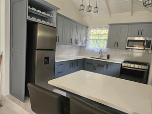 A kitchen with grey cabinets, a stainless steel refrigerator, a microwave, and a stove. - Synergy Suites Mt. Gay (Saint George)