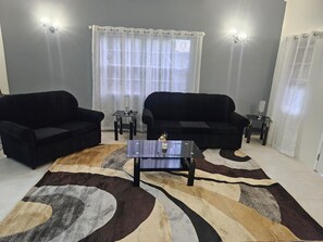 A living room with two black sofas, a coffee table, and a patterned rug. - Synergy Suites Mt. Gay (Saint George)