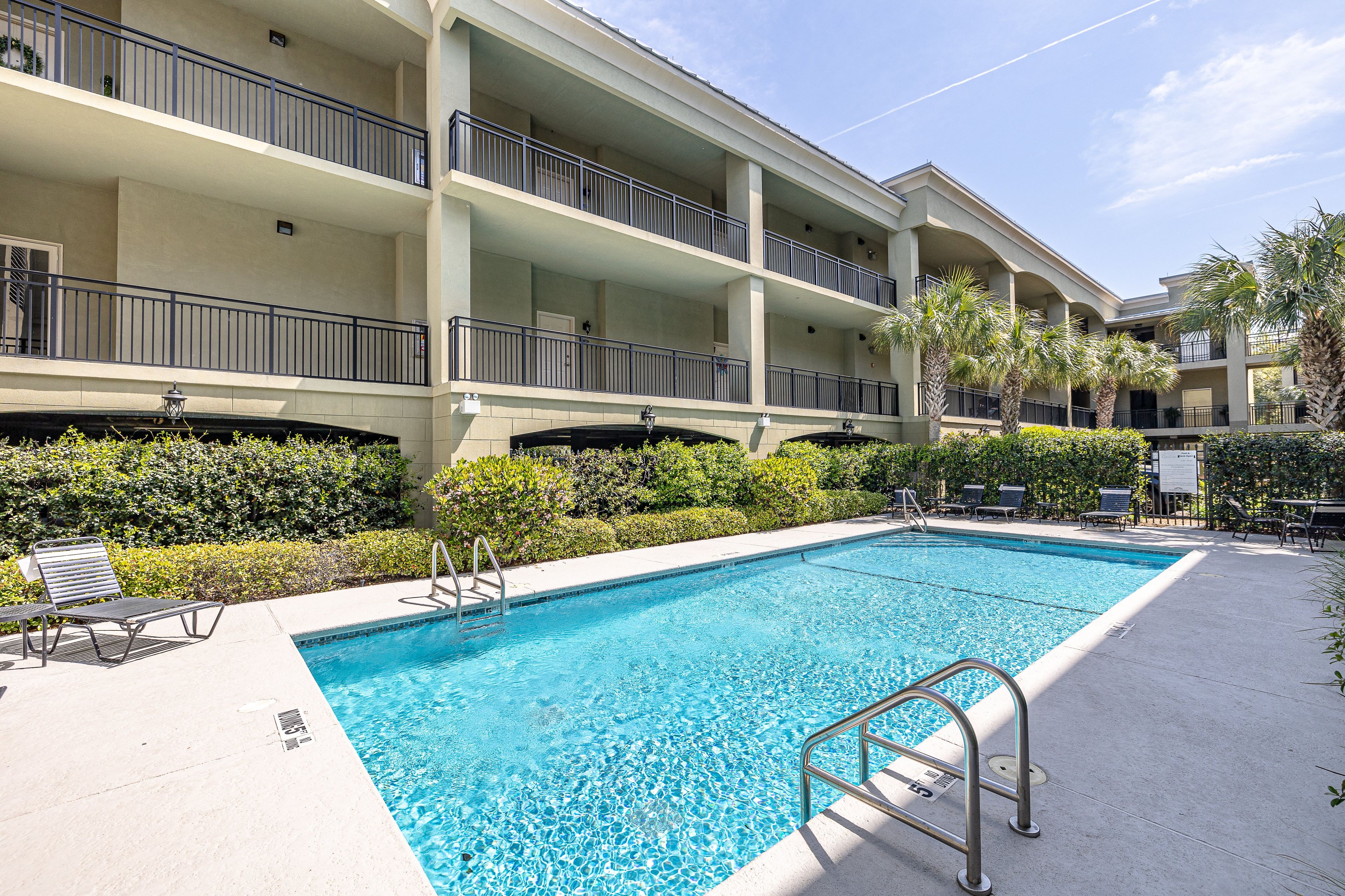 A hotel pool area with a clear blue pool, lounge chairs, and a multi-story building with balconies.