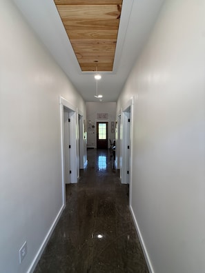 A hallway with white walls, a polished floor, and a wooden ceiling.