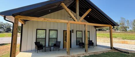 A covered outdoor seating area with a metal roof and wooden beams, adjacent to a building with large windows.