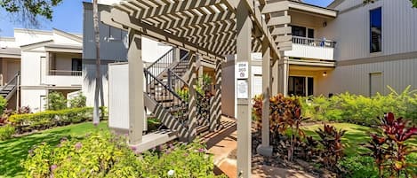 Un immeuble résidentiel doté d’un escalier extérieur abrité, d’une entrée sécurisée par un portail et d’un jardin bien entretenu.