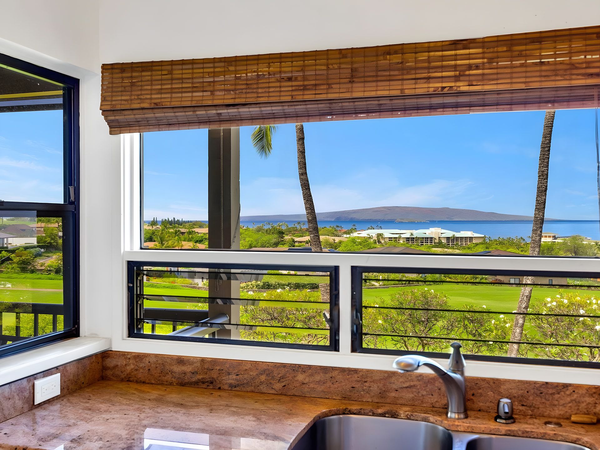 A kitchen with a view of a coastal landscape, including a body of water and palm trees.