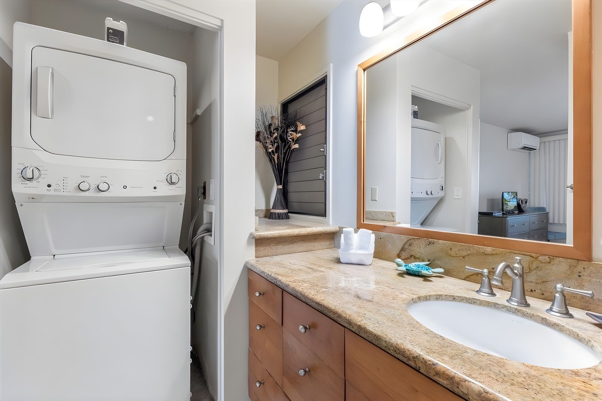 Een moderne badkamer met een ingebouwde wasmachine, een grote spiegel en een granieten aanrecht met een wastafel en badkamermeubel.