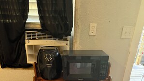 Ein Zimmer mit einem Holzbodenregal, auf dem eine schwarze Comafee-Mikrowelle und eine schwarze Kaffeemaschine stehen.