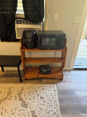 Una habitación con una estantería de madera que sostiene un microondas y una cafetera, ambos de color negro, de la marca Comafee.