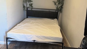 Ein kleines Schlafzimmer mit einem Bett, einem Nachttisch, einem Sessel und zwei Blumentöpfen.