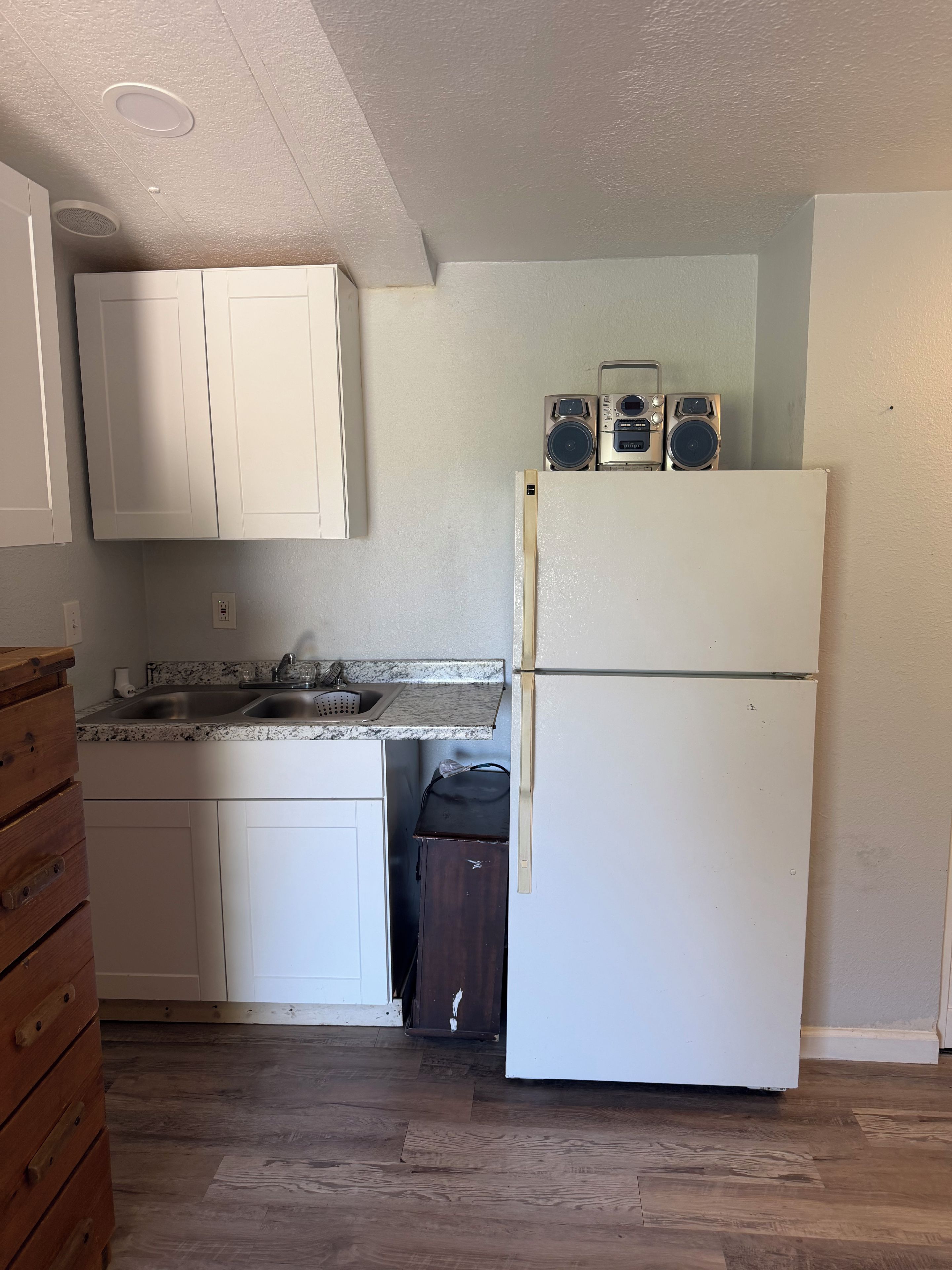 Una cocina con armarios blancos, un lavamanos doble, un refrigerador y un mueble de madera.