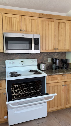 A kitchen with wooden cabinets, a microwave, a stove, a toaster, and a coffee maker. - Beautiful 2-bedroom house with AC in charming New Port Richey (New Port Richey)