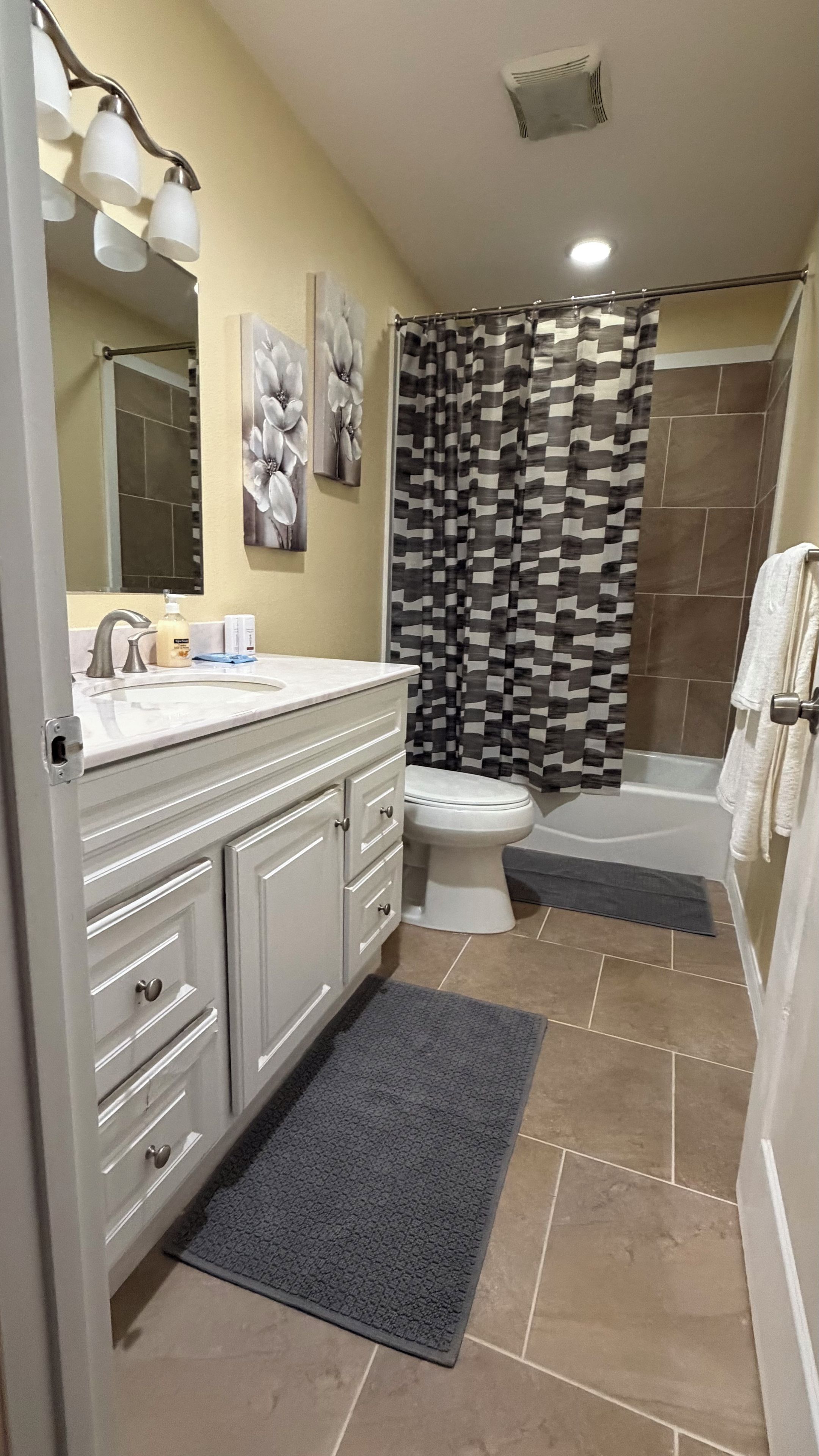 A bathroom with a white vanity, a toilet, a shower with a checkered curtain, and a towel rack.