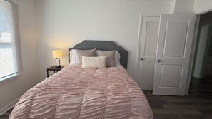 A bedroom with a bed, a bedside lamp, a door, and a window with blinds. - Beautiful 2-bedroom house with AC in charming New Port Richey (New Port Richey)