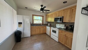 A kitchen with wooden cabinets, a white refrigerator, a microwave, a stove, and a ceiling fan. - Beautiful 2-bedroom house with AC in charming New Port Richey (New Port Richey)