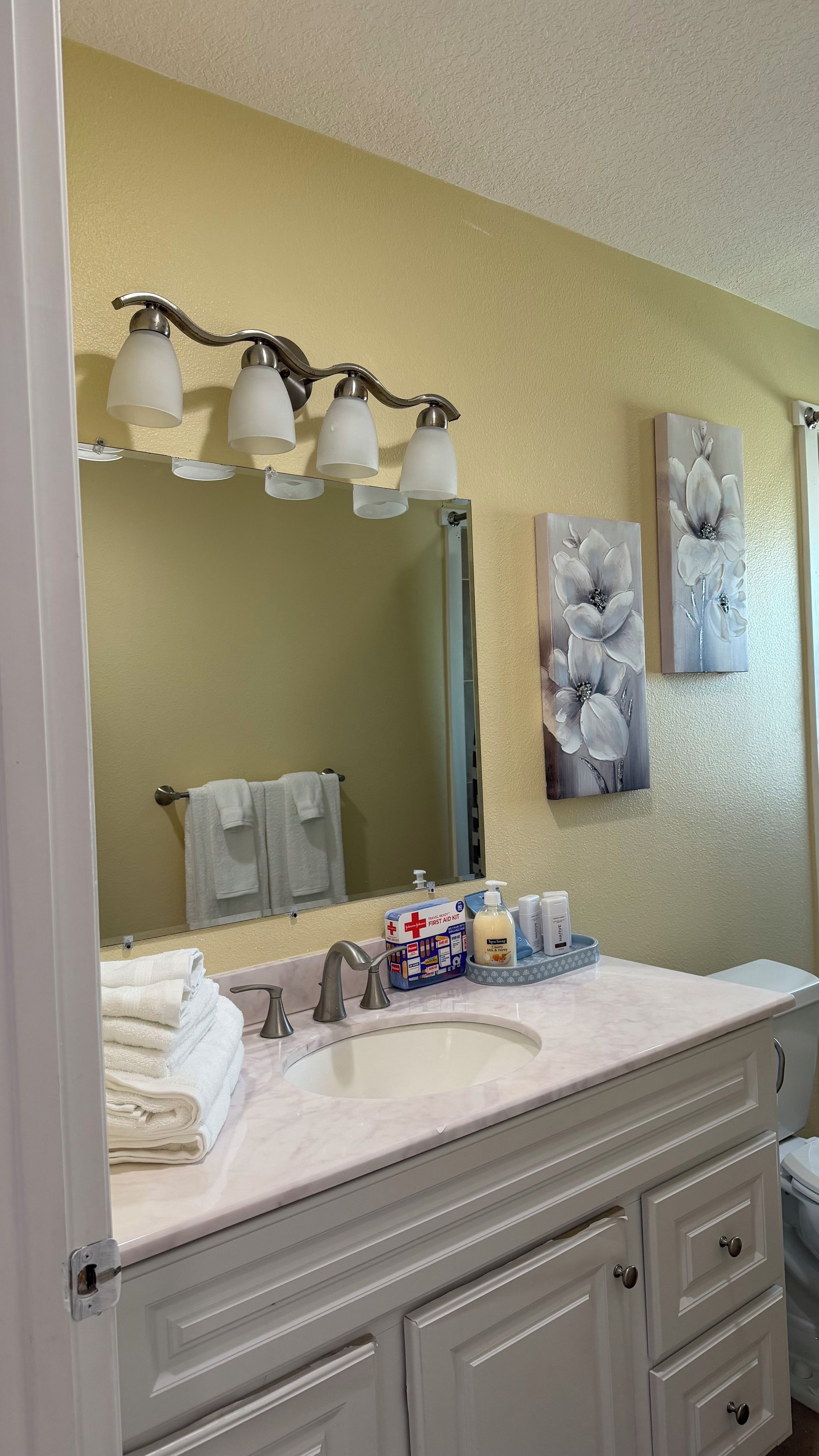 A bathroom with a large mirror, a vanity with a sink, and a first aid kit on the counter.