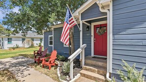 Ein Haus mit roter Tür, einer Veranda mit roten Adirondack-Stühlen und einer amerikanischen Flagge.
