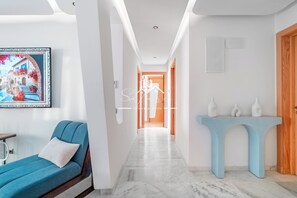 Ein modernes Hotelinterieur mit einer Diele, die zu einem Schlafzimmer führt, einem gerahmten Gemälde und einem Konsolentisch mit Vasen.