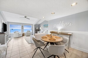 A modern living room with a dining area, large windows, and a ceiling fan. - Discover ocean views at Omni 1391 Shipwatch Circle, a 2-bed condo in Fernandina Beach. (Fernandina Beach)