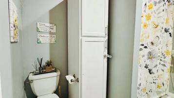 Une salle de bain avec des toilettes, un meuble blanc, un rideau de douche à motifs floraux et un panier de papier toilette.