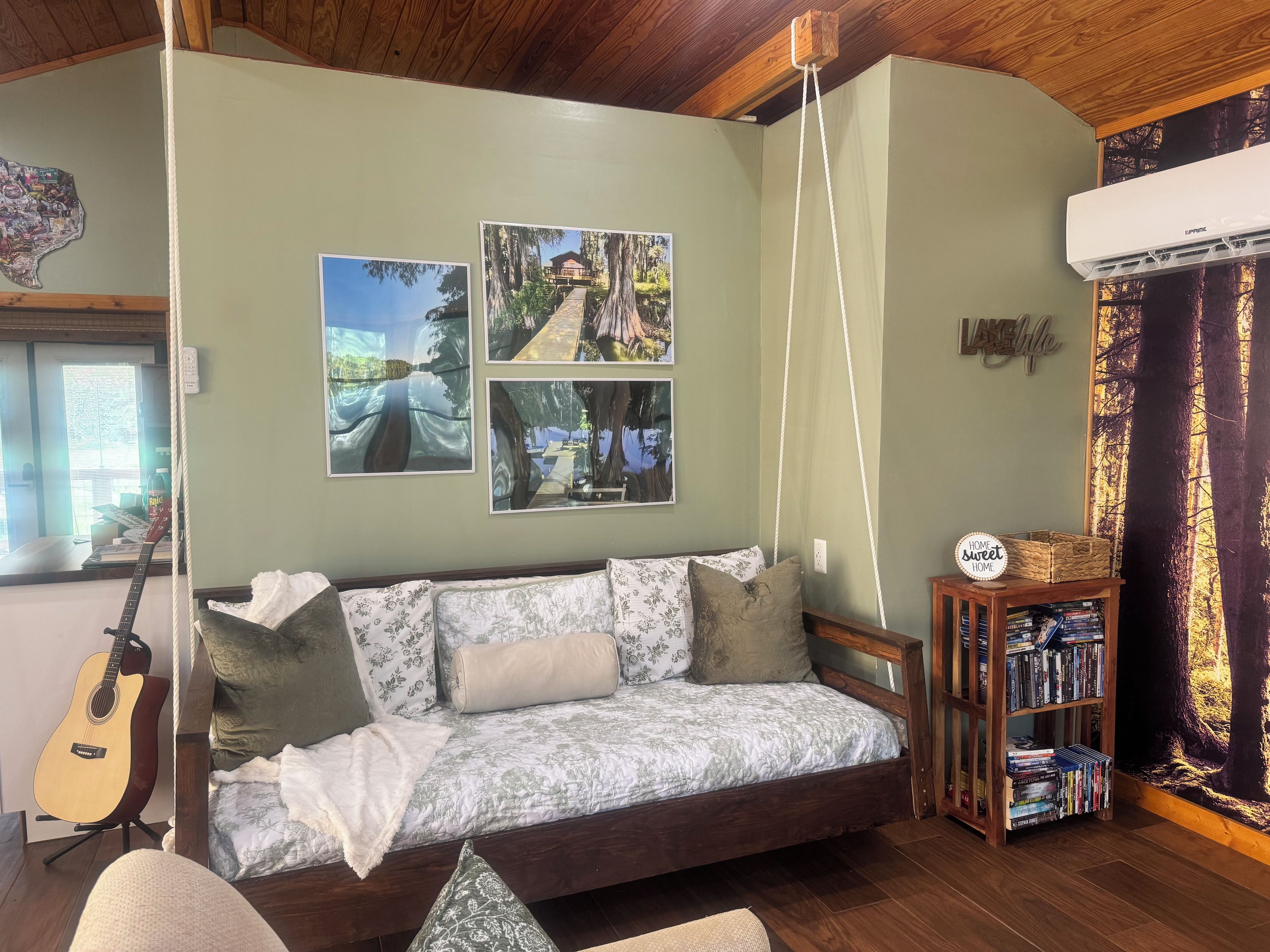 A cozy living room with a sofa, a guitar, a bookshelf, and framed pictures on the wall.