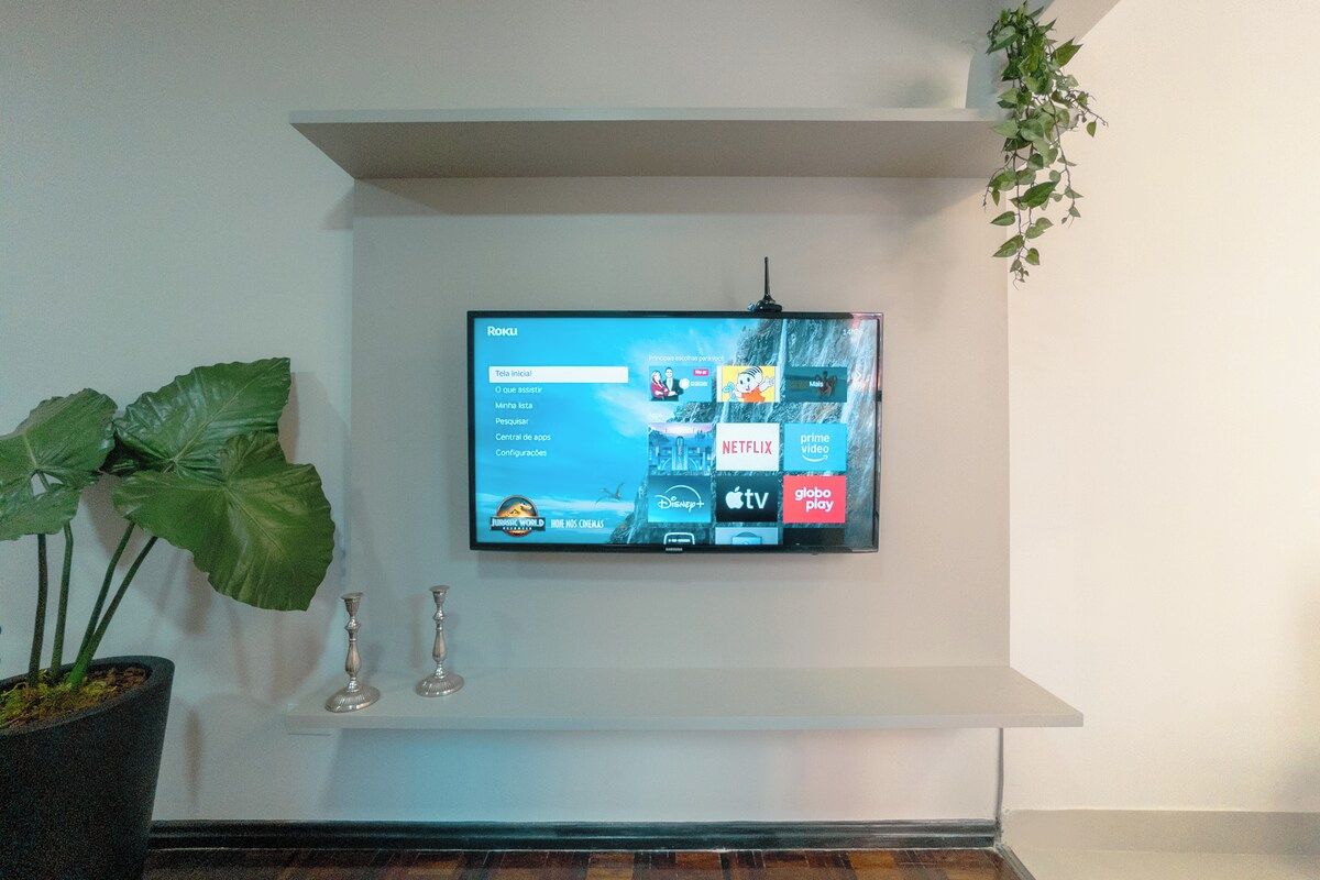 Ein Flachbildfernseher an der Wand montiert, darunter ein Regal mit verschiedenen Streaming-Diensten.