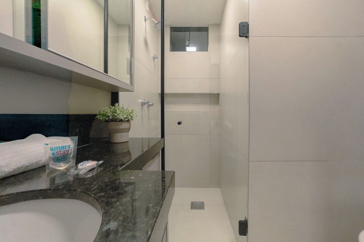 Casa de banho moderna com lavatório de mármore, uma pequena planta em vaso e cabine de duche em vidro.