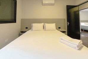 A hotel room with a large bed, a nightstand, a wall-mounted air conditioner, and a wardrobe. - Comfort and Top Location in Maringa - MJ41 (Maringá)