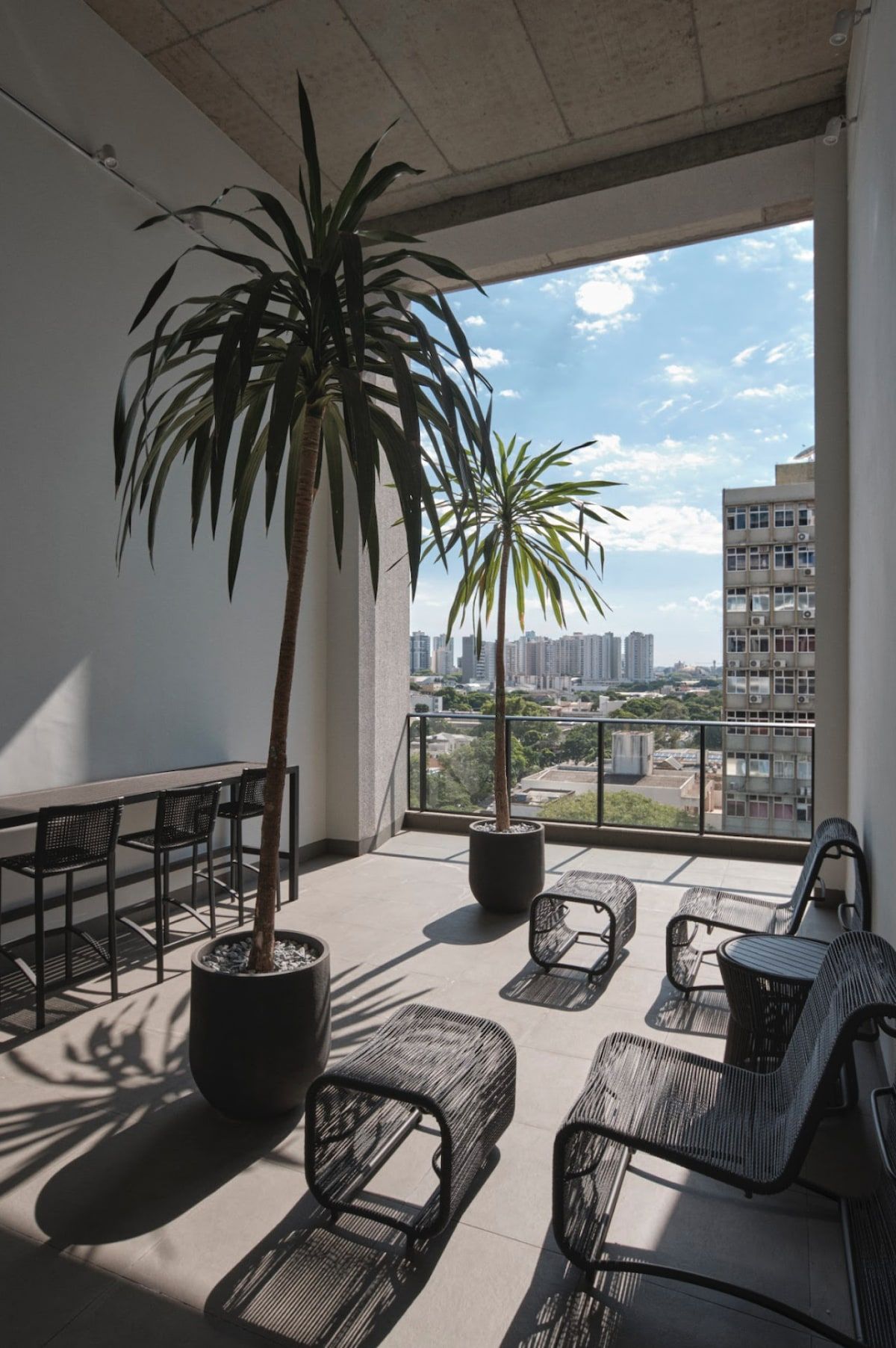A balcony with a view of a cityscape, furnished with chairs and tables, and two potted plants.