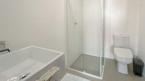 Un bany amb dutxa d'estuc de vidre, vàter blanc i banyera.