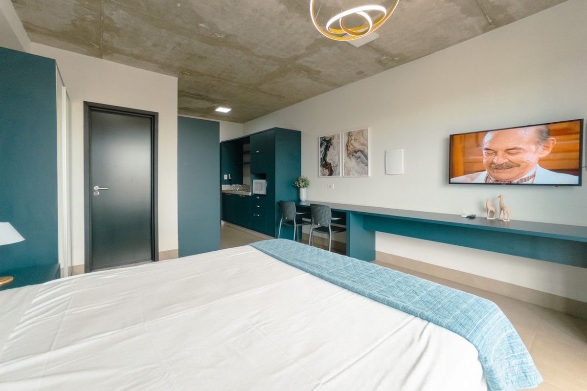 A modern bedroom with a bed, a desk, and a television on the wall.
